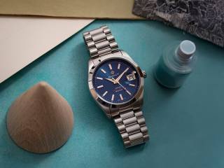 En silverklocka som ligger ner på ett bord med en blå urtavla från GANT.