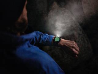 En man som kollar ner på sin Garmin-klocka som lyser upp mörkret , på urtavlan ser man en GPS.