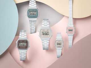 Fem Casio Vintage digitala klockor i olika färger, inklusive silver med grå urtavla, silver med ljusbeige urtavla, silver med brunröd urtavla, samt en mindre modell med silverlänk och rosa urtavla. Klockorna är arrangerade på en bakgrund med vågiga former i pastellfärger som rosa, beige och ljusblått.