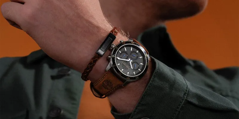 en man i grön skjorta har en timberland klocka med svart urtavla och brunt läderarmband