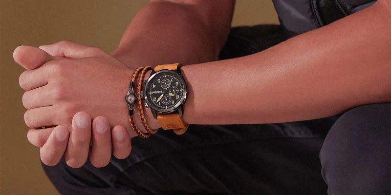 en man har en svart timberlandklocka med brunt läderarmband på handleden