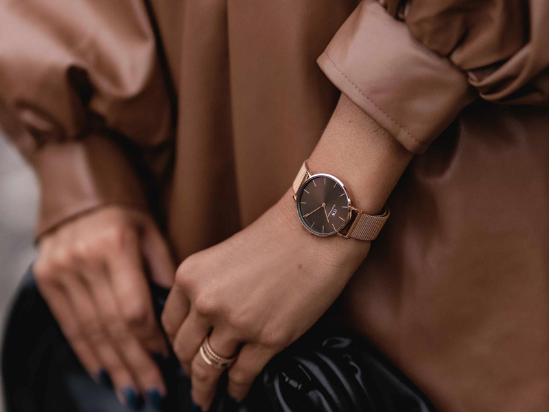 En kvinna som visar upp sina båda händer med en beige klocka från Daniel Wellington.